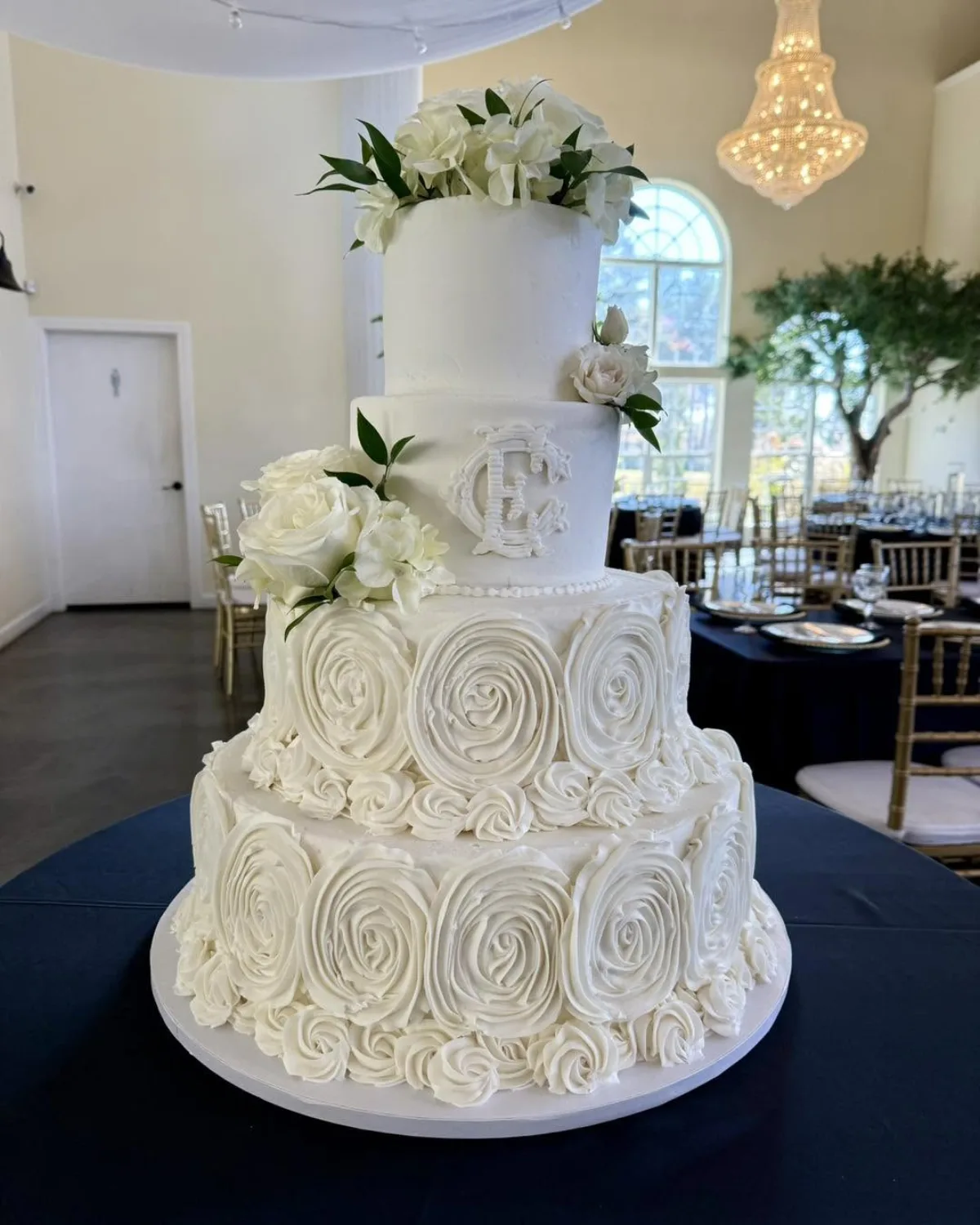 A white four-tier wedding cake with buttercream rosettes and fresh white roses